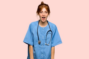 Genç Kızıl saçlı hemşireyle sürpriz ve pembe bir arka plan üzerinde şok yüz ifadesi