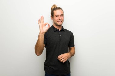 Parmaklar ok işaretiyle gösterilen beyaz duvarın üzerinden uzun saçlı sarışın adam