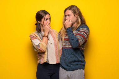 Biraz gergin ve korkmuş ellerini ağzına koyarak hippi çift sarı arka plan üzerinde