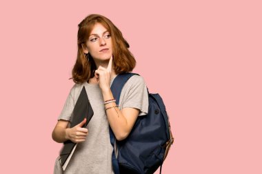Pembe arka plan üzerinde ararken bir fikir düşünme genç redhead öğrenci