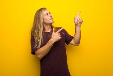 İşaret parmağı ile işaret ve ararken sarı duvarın üzerinden uzun saçlı sarışın adam
