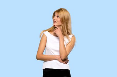 Genç sarışın kadın izole mavi arka plan üzerinde ararken bir fikir düşünüyorum