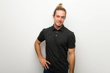 Silah, kalça ile poz ve gülümseyen beyaz duvarın üzerinden uzun saçlı sarışın adam