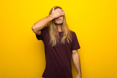 Sarı duvar eller tarafından gözleri kaplama üzerinde uzun saçlı sarışın adam. Bir şey görmek istiyor musunuz