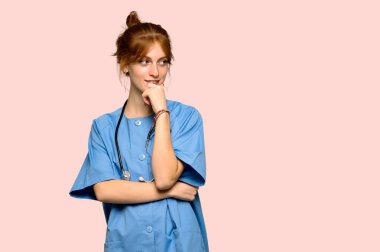 Genç redhead hemşire tarafına el ile çeneme pembe arka plan üzerinde seyir