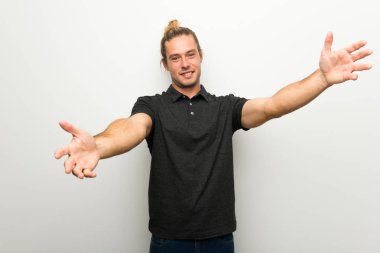 Sunulması ve el ile gelmek davet beyaz duvarın üzerinden uzun saçlı sarışın adam