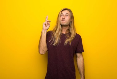 En iyi dilek ve geçiş parmaklarıyla sarı duvarın üzerinden uzun saçlı sarışın adam