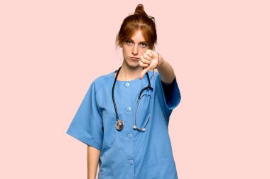 Başparmak işareti negatif ifade ile aşağı pembe arka plan üzerinde gösterilen genç redhead hemşire