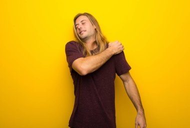 Bir çaba yapılmış olması için omuz ağrısı muzdarip sarı duvarın üzerinden uzun saçlı sarışın adam