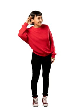 Kırmızı kazaklı bir şey izole beyaz arka plan üzerinde kulak el koyarak dinleme kısa saçlı kızla tam uzunlukta bir kadeh