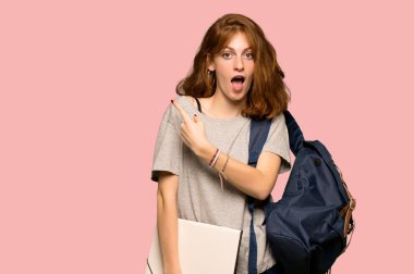 Şaşırttı ve yan pembe arka plan üzerinde işaret genç redhead öğrenci