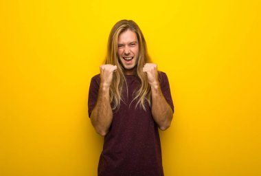 Kazanan konum bir zaferini kutluyor sarı duvarın üzerinden uzun saçlı sarışın adam