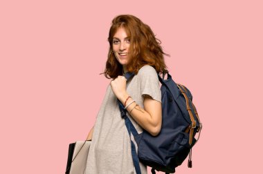 Silah, kalça ile poz ve pembe arka plan üzerinde gülüyor genç redhead öğrenci