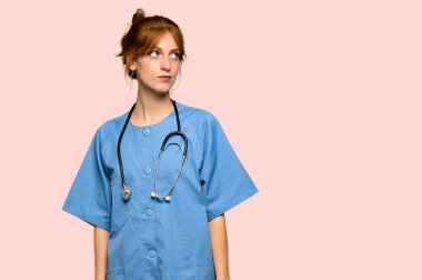 Pembe arka plan üzerinde ciddi bir yüz ile ararken genç redhead hemşire