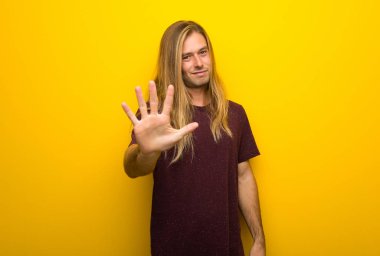Beş parmak ile sayma sarı duvarın üzerinden uzun saçlı sarışın adam