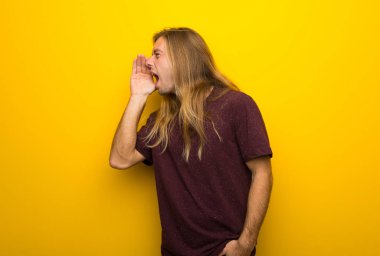 Lateral için açık ağızlı bağırmayı sarı duvarın üzerinden uzun saçlı sarışın adam
