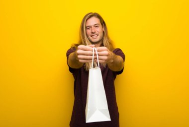 Bir sürü alışveriş torbaları tutan sarı duvarın üzerinden uzun saçlı sarışın adam