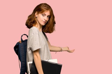 Geri işaret ve pembe arka plan üzerinde bir ürün sunma genç redhead öğrenci