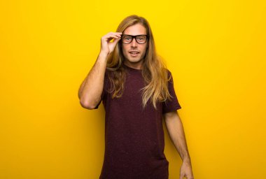 Gözlüklü ve sürpriz sarı duvarın üzerinden uzun saçlı sarışın adam