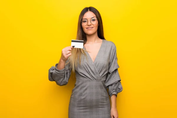 Młoda Kobieta Okularami Żółte Ściany Trzymając Kartę Kredytową — Zdjęcie stockowe