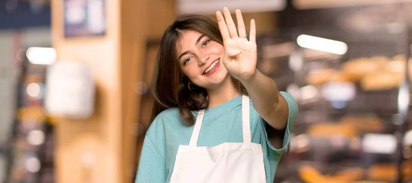 Girl with apron happy and counting four with fingers in a bakery