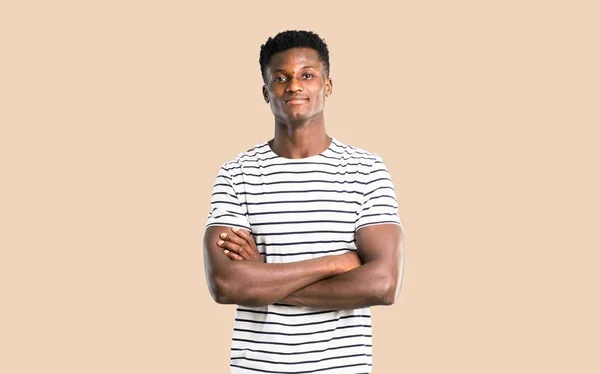 Dark skinned man with striped shirt keeping the arms crossed in frontal position. Confident expression on isolated ocher background