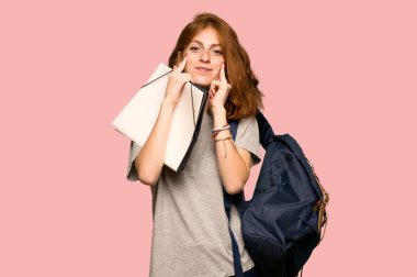 Pembe arka plan üzerinde mutlu ve keyifli bir ifadeyle gülümseyen genç redhead öğrenci