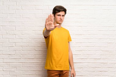 Genç adam yanlış düşünüyor bir durum inkar durdurmak jest yapma beyaz tuğla duvarın üzerinden