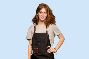 Silah, kalça ile poz ve mavi arka plan üzerinde gülümseyen önlük ile genç Kızıl saçlı kadın