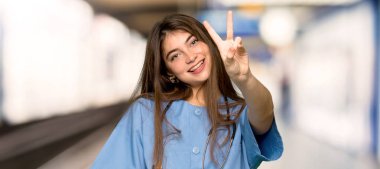 Genç gülümseyen ve zafer işaret gösteren bir hastanede hemşire