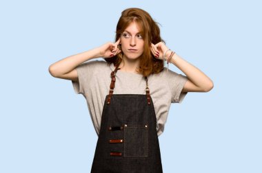 Her iki kulak elleri ile mavi arka plan üzerinde kapsayan önlük ile genç Kızıl saçlı kadın