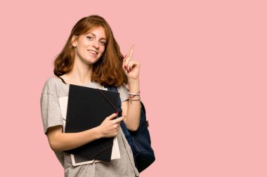 İşaret parmağı ile işaret ve pembe arka plan üzerinde ararken genç redhead öğrenci