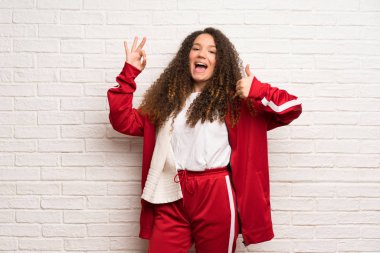 Kıvırcık saçlı gösteren ok işareti ile ve jest bir başparmak veren ile genç spor kız