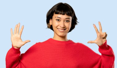 Kısa saçlı kız kırmızı kazaklı sekiz ile izole mavi zemin üzerine parmak sayma