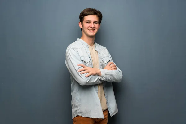 Teenager man with jean jacket over grey wall with arms crossed and looking forward