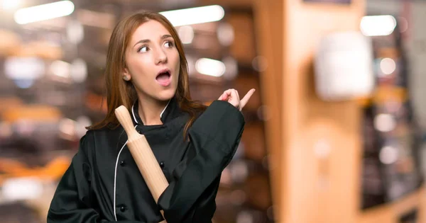 Young redhead chef woman thinking an idea pointing the finger up in the bakery