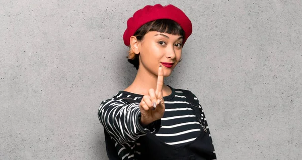 ベレー帽を示すと織り目加工の壁に指を離すと若い女性 — ストック写真