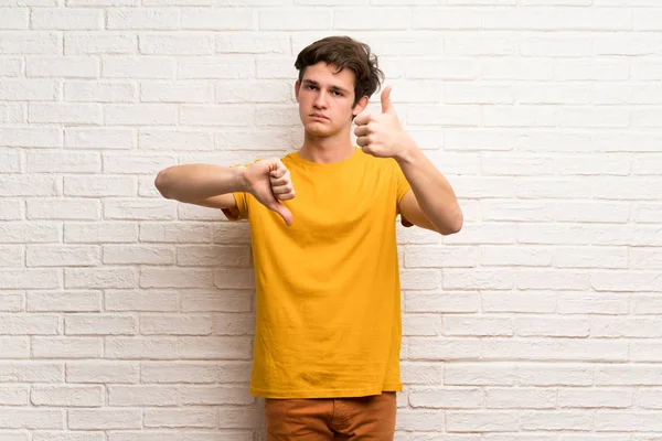 Adolescente Homem Sobre Parede Tijolo Branco Fazendo Bom Mau Sinal — Fotografia de Stock
