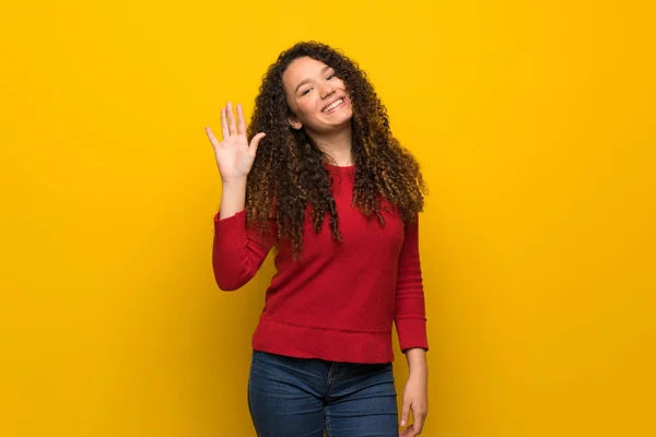 Chica Adolescente Con Suéter Rojo Sobre Pared Amarilla Saludando Con —  Fotos de Stock