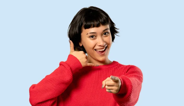 電話のジェスチャーを作ると 分離された青の背景に正面を指している赤いセーターと短い髪の女の子 — ストック写真