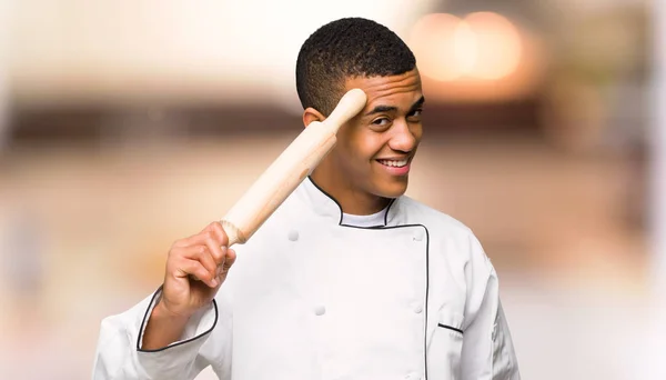 Young afro american chef man saluting with hand on unfocused background