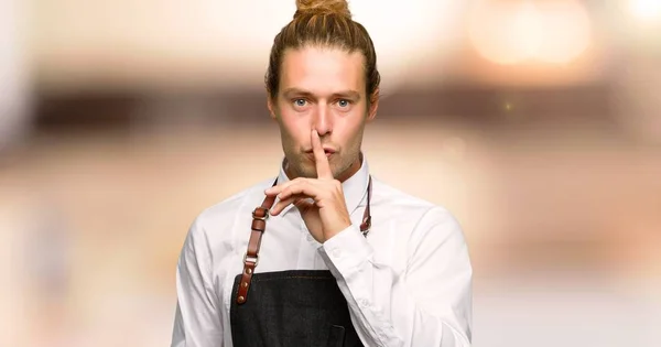 Barber man in an apron showing a sign of silence gesture putting finger in mouth in a barber shop