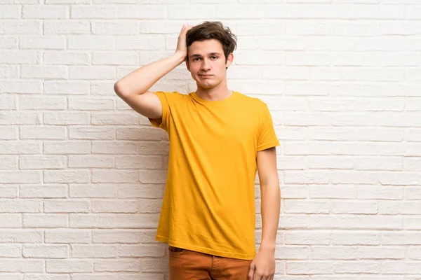 Teenager man over white brick wall with an expression of frustration and not understanding