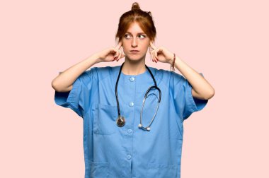 Her iki kulak elleriyle pembe arka plan üzerinde kapsayan genç redhead hemşire