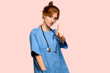 Gösterilen ve pembe arka plan üzerinde parmak kaldırma genç redhead hemşire