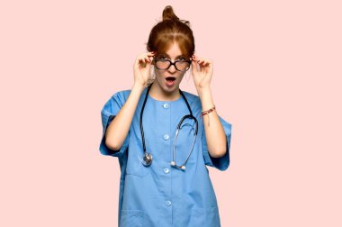 Genç redhead hemşire gözlüklü ve pembe bir arka plan üzerinde sürpriz
