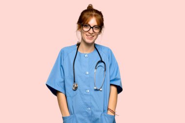 Genç redhead hemşire gözlüklü ve pembe bir arka plan üzerinde mutlu