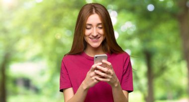 Genç Kızıl saçlı kız parkta mobil ileti gönderme