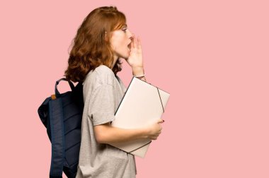 Ağzınla lateral için açık pembe arka plan üzerinde bağırarak genç redhead öğrenci