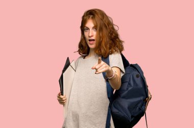 Size genç redhead öğrenci puan parmak pembe bir arka plan üzerinde kendine güvenen bir ifade ile